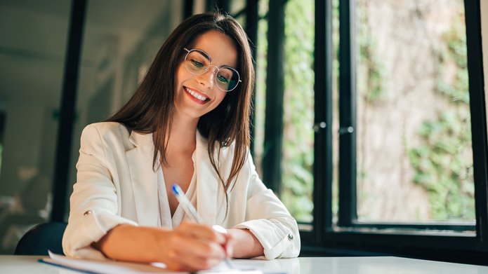 Portrait of a female student filling questionnaire while sitting at desk at university. Zdjęcie uśmiechniętej kobiety piszącej egzamin