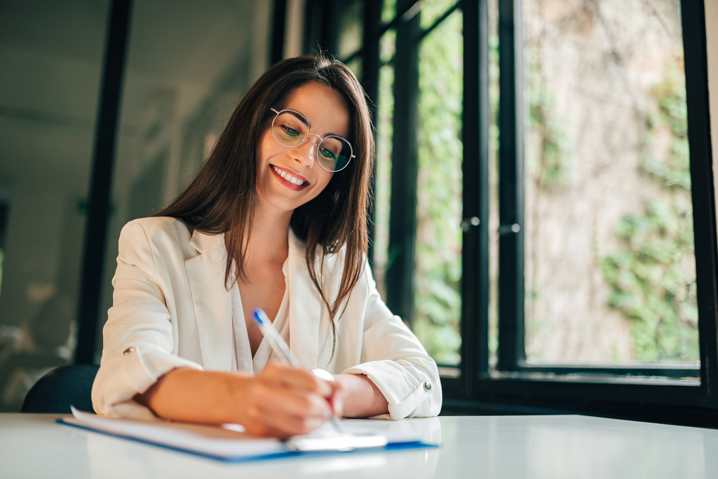 Portrait of a female student filling questionnaire while sitting at desk at university. Zdjęcie uśmiechniętej kobiety piszącej egzamin